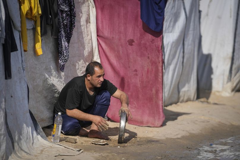 رجل يغسل صينية في مخيم للنازحين الفلسطينيين بدير البلح، وسط قطاع غزة، الجمعة 17 يناير 2025. 