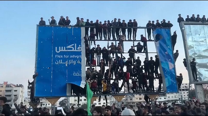 العشرات من الفلسطينيين يعتلون لوحنة إعلانات ضخمة عند مفترق السرايا بمدينة غزة وقت قيام حماس بتسليم 3 أسرى إسرائيليات لمنظمة الصليب الأحمر