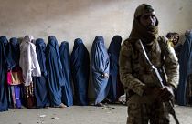 A Taliban fighter stands guard as women wait to receive food rations distributed by a humanitarian aid group in Kabul, 23 May, 2023