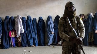 A Taliban fighter stands guard as women wait to receive food rations distributed by a humanitarian aid group in Kabul, 23 May, 2023