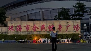 FILE - A woman stands near flowers placed outside the "Zhuhai People's Fitness Plaza", where a man deliberately rammed his car into people exercising at the sports centre.