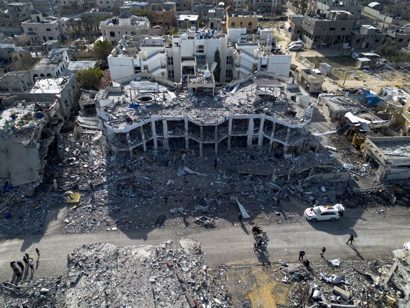 فلسطينيون يسيرون وسط الدمار الذي خلفته الإسرائيلية بالقرب من مستشفى النجار في رفح بقطاع غزة مع دخول اتفاق وقف إطلاق النار حيز التنفيذ 19 كانون الثاني يناير 2025