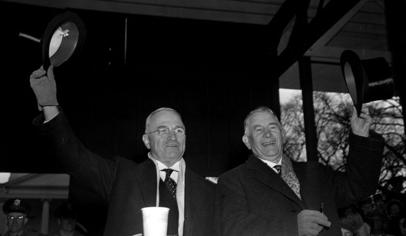 Harry S. Truman, left, and Vice President Alben W. Barkley wave from the inaugural parade reviewing stand in front of the White House after their inauguration in Washington