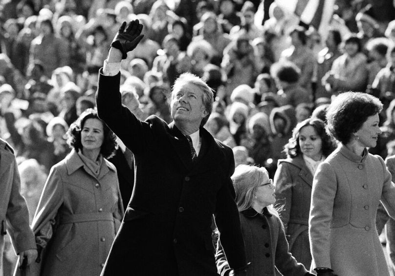 Jimmy Carter waves to the crowd while walking with his wife Rosalynn along Pennsylvania Avenue and their daughter Amy