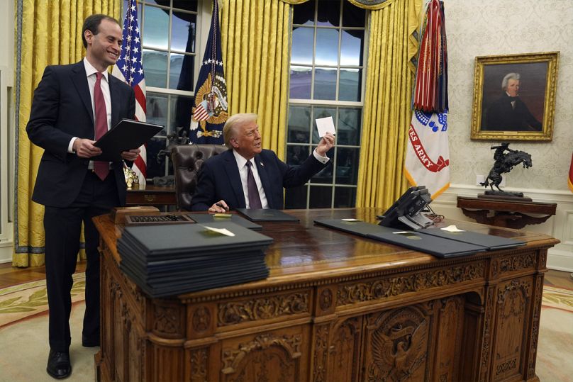 Presidente Donald Trump segura uma carta do antigo Presidente Joe Biden enquanto assina ordens executivas na Sala Oval da Casa Branca, segunda-feira, 20 de janeiro de 2025