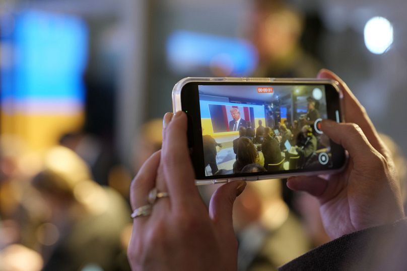 A woman films with her mobile phone as people watch the inauguration of Donald Trump at the Ukraine house alongside the World Economic Forum in Davos, Monday, Jan 20, 2025