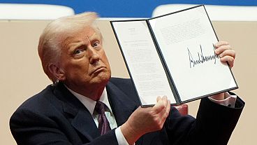 President Donald Trump holds up an executive order after signing it at an indoor Presidential Inauguration parade event in Washington, Monday, Jan. 20, 2025.