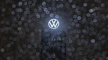 Raindrops collect on the windshield of a car while the logo on the roof of the Volkswagen brand tower shines behind. Wolfsburg, Germany. 9 December 2024.