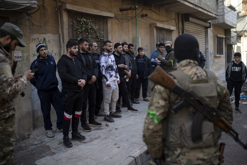 أشخاص يقفون في طابور قبل أن يقوم أفراد من قوات الأمن الجديدة بالتحقق من هوياتهم  حمص، سوريا، الخميس، 2 يناير/كانون الثاني 2025