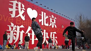 Chinese people play shutter cock near a huge display board with the words, "I Love Beijing, Happy New Year 2025," in Beijing