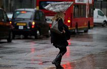 A woman's umbrella is blown inside out as she walks through a heavy rain shower in the Canary Wharf business district of London, Wednesday, Nov. 20, 2013.