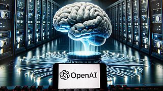 The OpenAI logo is seen displayed on a cell phone with an image on a computer monitor generated by ChatGPT's Dall-E text-to-image model, Friday, Dec. 8, 2023, in Boston.