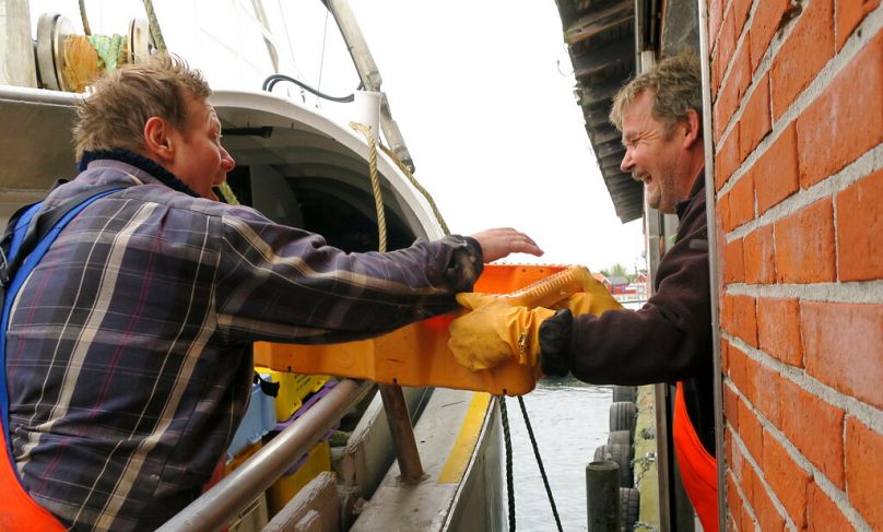 Ulrik Koelle Hansen, left, hands over a crate with plaices to a warehouse employee in Bagenkop, Denmark, October 2016