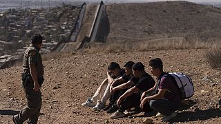 A border patrol officer walks past four men detained after crossing the border illegally