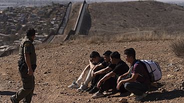 A border patrol officer walks past four men detained after crossing the border illegally