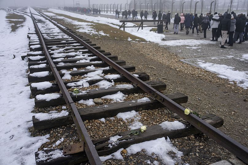 Visitantes caminham ao longo dos carris dos caminhos-de-ferro outrora utilizados para transportar judeus de toda a Europa para Auschwitz, 23/01/2025