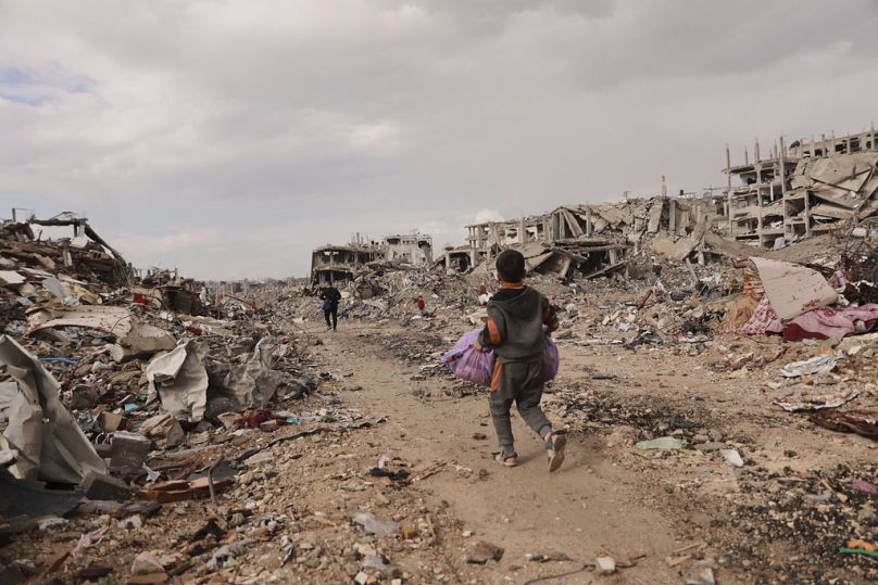 A Palestinian boy carries his belongings as he walks with his family next to the rubble of destroyed homes, after the ceasefire deal between Israel and Hamas, in Gaza City