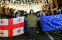 Demonstrators hold a Georgian national and an EU flag as they listen to outgoing Georgian President Salome Zourabichvili during an anti-government rally outside parliament