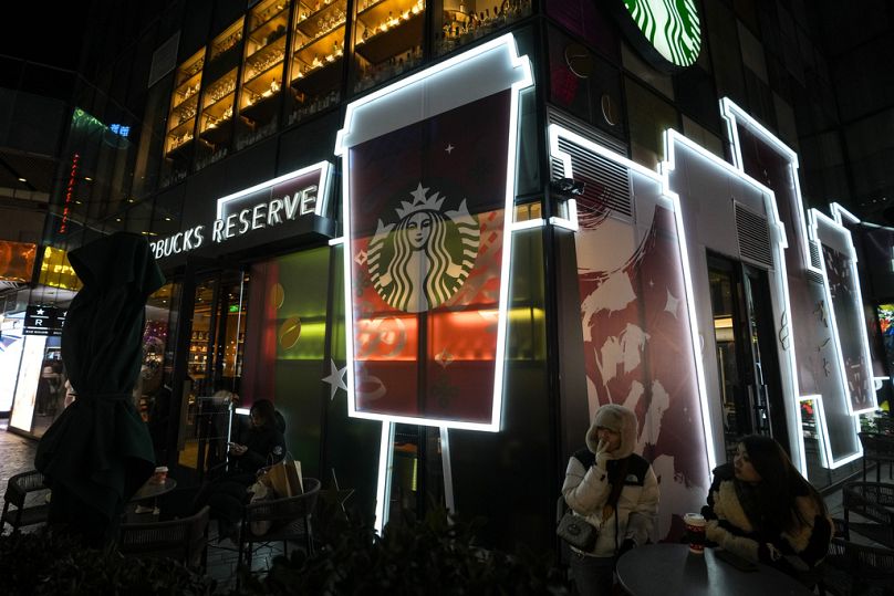 Persone bevono un caffè fuori da uno Starbucks in un centro commerciale di Pechino, 23 dicembre 2023