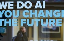 A woman is reflected in a window with a slogan about AI ahead of the World Economy Forum in Davos, Switzerland, Sunday, Jan. 19, 2025.