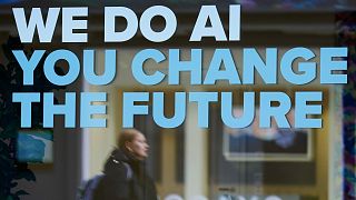 A woman is reflected in a window with a slogan about AI ahead of the World Economy Forum in Davos, Switzerland, Sunday, Jan. 19, 2025.