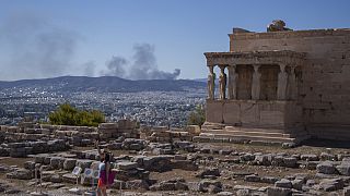 Una donna posa per una foto davanti alle statue delle Cariatidi che sorreggono il portico del tempio Eretteo di Atene, risalente al V secolo a.C..