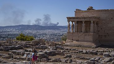 A woman poses for a photo in front Caryatid statues that prop up the porch of the 5th century B.C. Erechtheion temple in Athens.