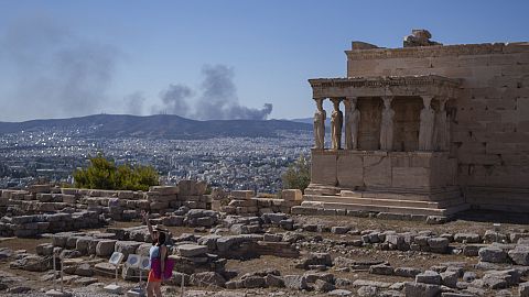 A woman poses for a photo in front Caryatid statues that prop up the porch of the 5th century B.C. Erechtheion temple in Athens.