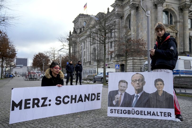Protestujący trzymają banery krytykujące politykę Friedricha Merza.