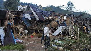 10 Ekim 2023 Salı günü Myanmar'ın Laiza kentindeki Mung Lai Hkyet yerinden edilme kampında biri, hava ve topçu saldırıları sonrasında yıkılan evlere bakıyor
