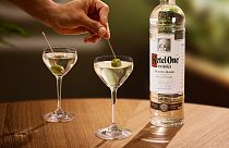 A bottle of Ketel One vodka and two dirty martinis on a table. 