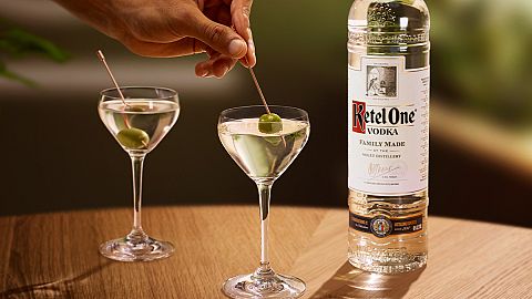 A bottle of Ketel One vodka and two dirty martinis on a table. 