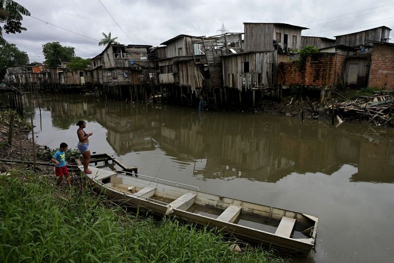 A mother and son walk on the bank of the Tucunduba Channel where stilt homes stand in the Terra Firme neighboyrhood of Belem, Brazil