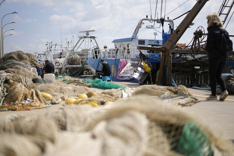 Fishermen mend nets in front of fishing boats at harbor in the Roman port of Fiumicino.