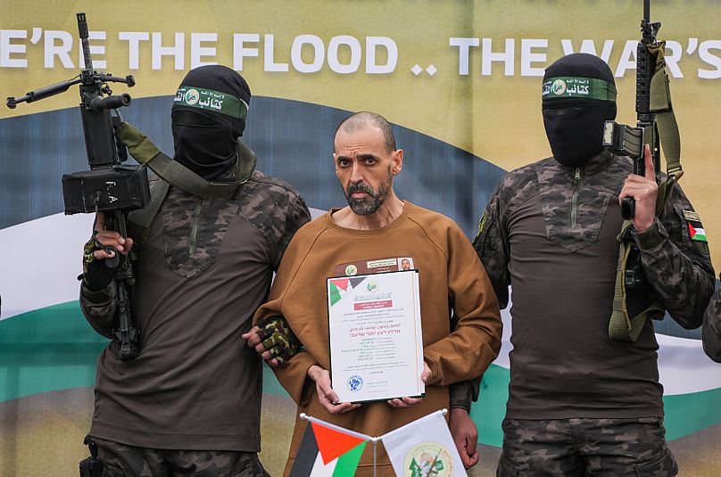 Eli Sharabi stands on a stage escorted by Hamas fighters before being handed over to the Red Cross in Deir al-Balah, 8 February, 2025