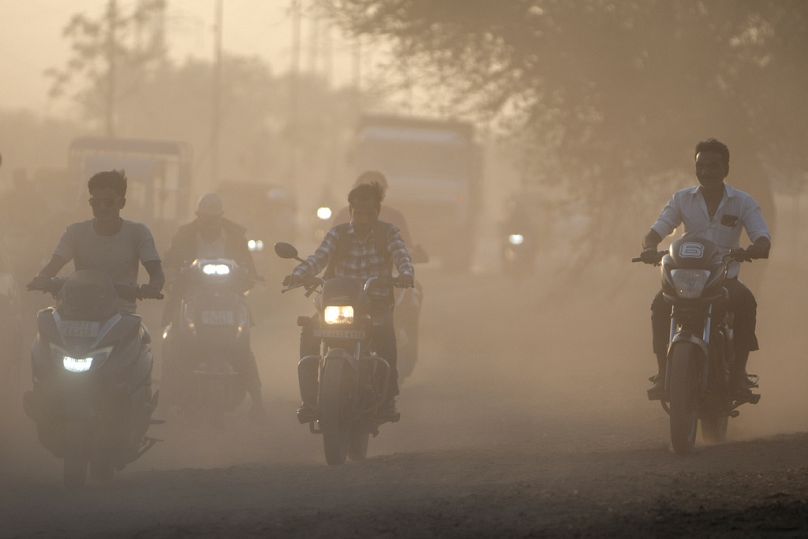 Dust rises as commuters drive past a road in Ahmedabad, India.