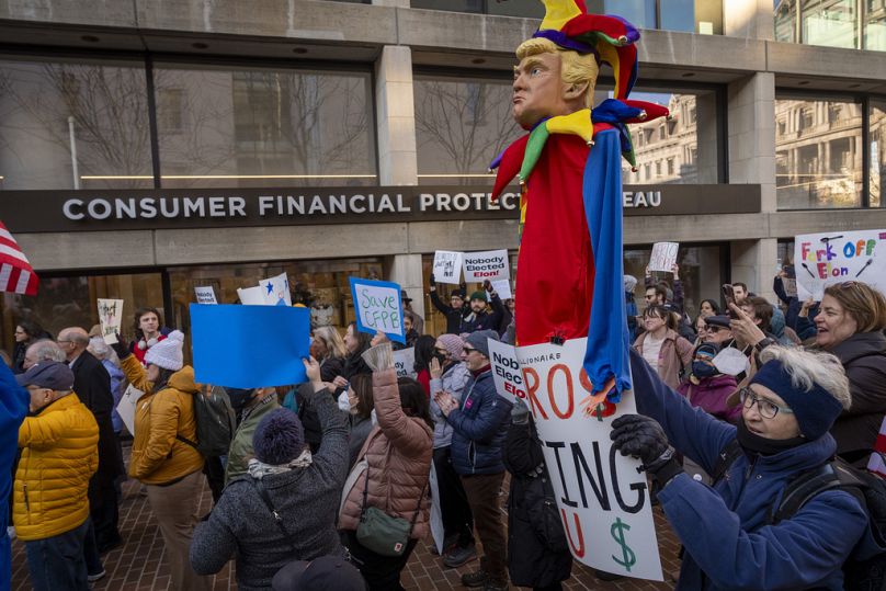 A retired worker with USAID, holds a jester puppet representing President Donald Trump, as she attends a protest in support of the CFPB, Monday, Feb. 10, 2025