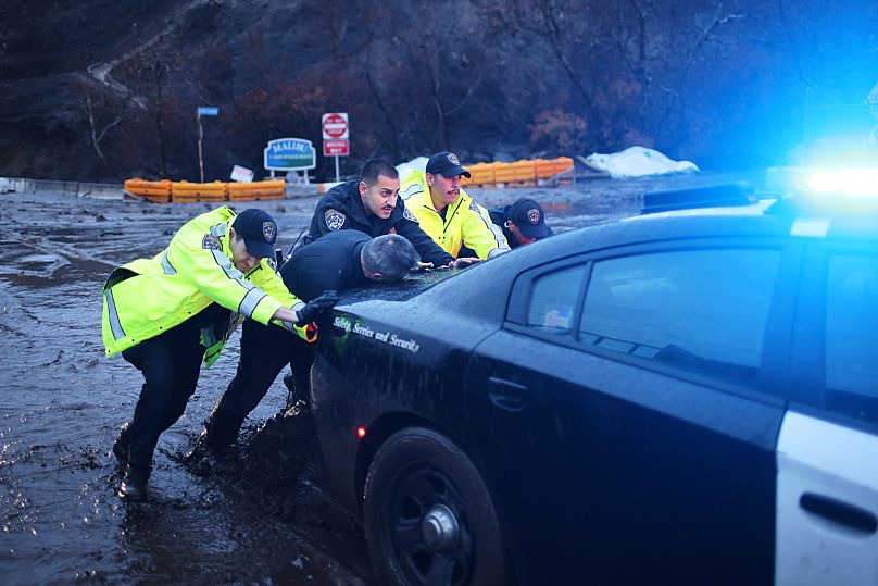 ضباط شرطة يدفعون سيارة طوارئ عالقة في الوحل في منطقة حرائق باليسيدس خلال عاصفة يوم الخميس 13 فبراير/شباط 2025 في ماليبو، كاليفورنيا.