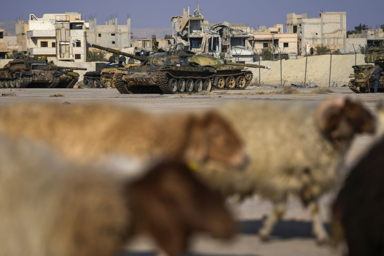 Sheep pass by tanks that belonged to the ousted Assad government, parked in front of a destroyed building in Palmyra, Syria.