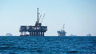 Cargo vessels are seen anchored offshore, sharing space with oil platforms off the coast of California. 