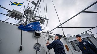 El capitán Thomas Zimmerman, a la derecha, da la orden de izar la bandera de la OTAN en el patrullero HMS Carlskrona (P04) que zarpa del puerto naval de Karlskrona, Suecia.