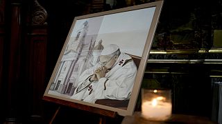 A candle glimmers alongside a painting of Pope Francis at San José de Flores basilica, Buenos Aires, Argentina, where he worshipped as a youth, Sunday, Feb. 23, 2025. 