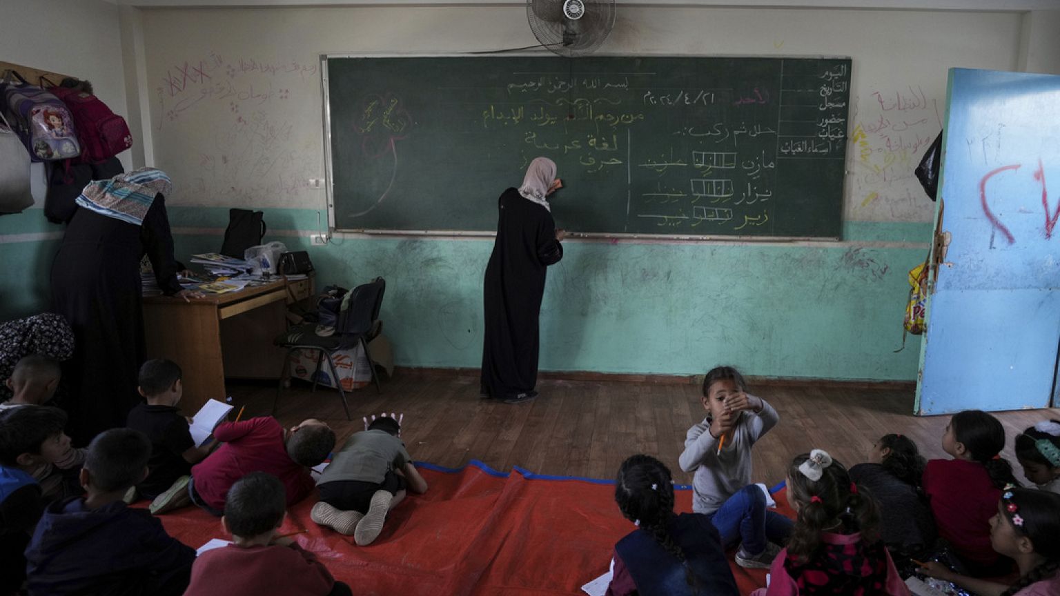 Un profesor con niños en una clase improvisada en Deir al-Balah, recientemente invadida por tierra, el domingo 21 de abril de 2024.