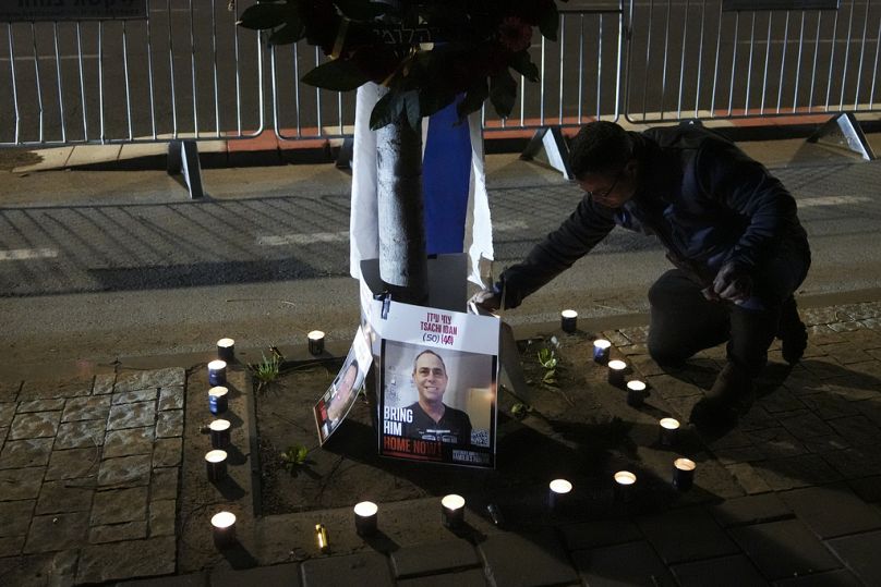 Mężczyzna zapala świece i pokazuje zdjęcia czterech nieżyjących izraelskich zakładników przekazanych Izraelowi, przed Instytutem Medycyny Sądowej Abu Kabira