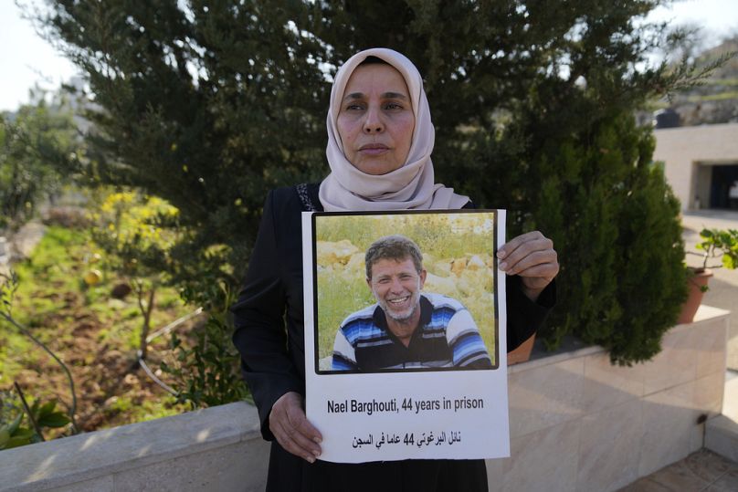 الفلسطينية إيمان البرغوثي، زوجة الأسير في إسرائيل نائل البرغوثي تحمل ملصقًا يحمل صورة لزوجها  قرية كوبر بالضفة الغربية شمال رام الله يوم السبت، 18 يناير 2025
