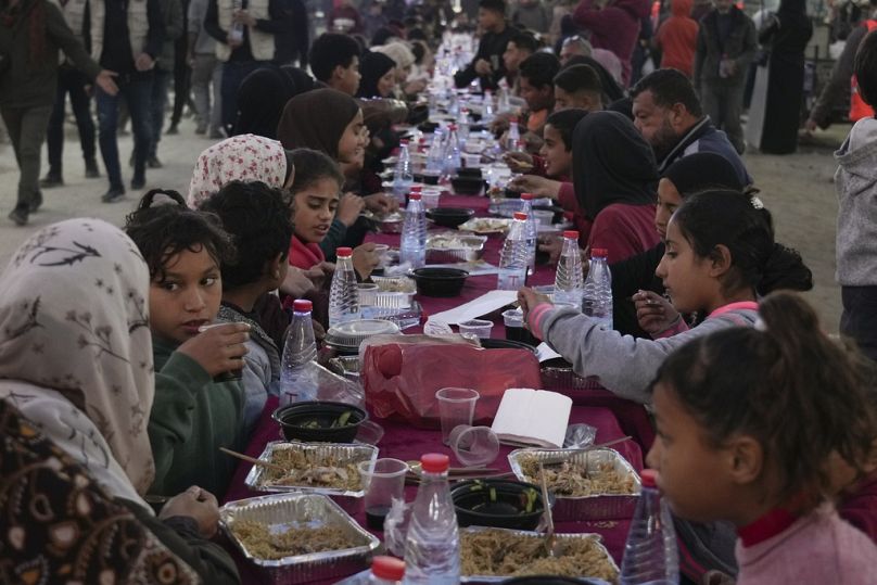 فلسطينيون يجتمعون حول طاولة محاطة بأنقاض المنازل المدمرة لتناول وجبة الإفطار، في أول أيام شهر رمضان، في رفح جنوب قطاع غزة، في 1 مارس 2025.