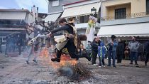 A man dressed in animal skins and heavy bronze bells, jumps over a burning carnival effigy during carnival celebrations in Distomo