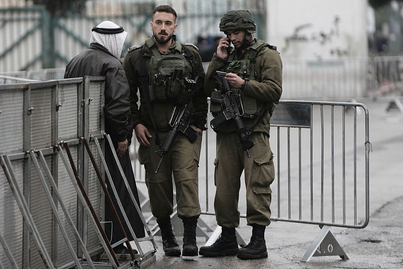 جنود إسرائيليون يدققون في هوية رجل فلسطيني عند نقطة تفتيش وهو في طريقه إلى حرم المسجد الأقصى في القدس لأداء صلاة الجمعة الأولى من شهر رمضان، 7 مارس/آذار 2025