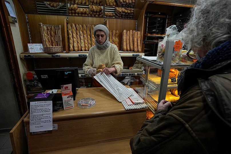 Mylene Poirier coloca baguetes num saco para um cliente numa padaria, em Versailles, a oeste de Paris, terça-feira, 29 de novembro de 2022. 