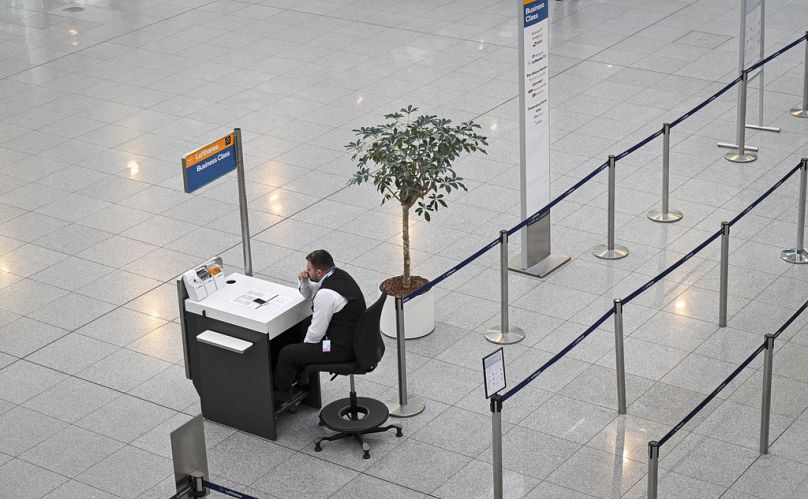 An airport employee sits in front of an empty check-in counter at Terminal 2 at Munich Airport.